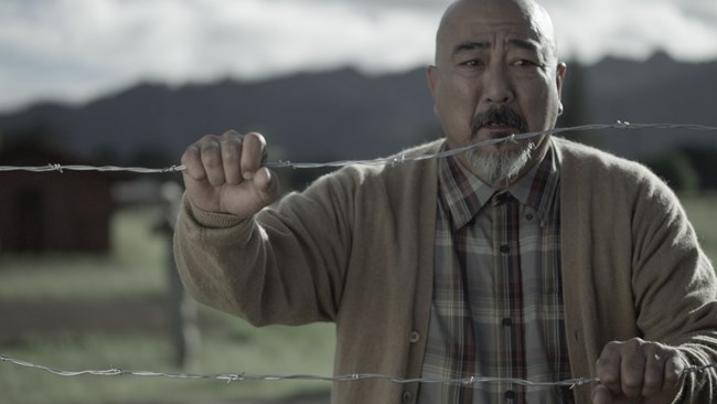 An Asian man behind a barbed wire fence with an anguished expression on his face.