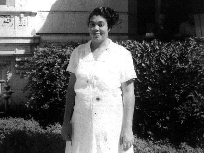 An African American woman wears an all-white uniform while standing outside.