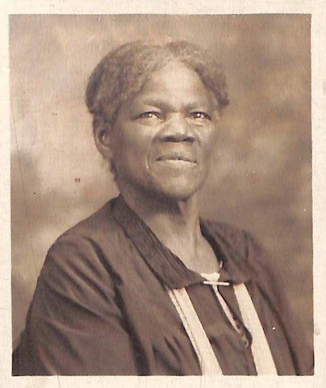 An African American woman with gray hair wears a black shirt with two white stripes.