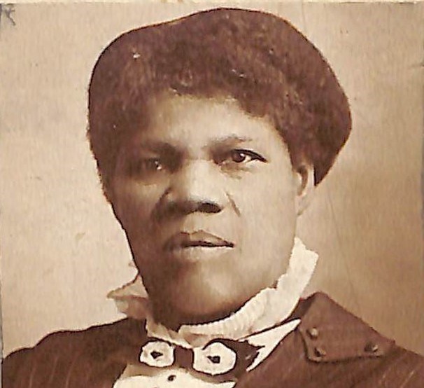 An African American woman wears a white shirt with black buttons, a black and white bow tie, and a pinstripe jacket