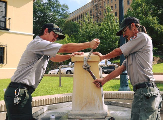 Two park rangers work on fixing one of the thermal drinking fountains at the park.