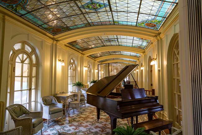 A grand piano with white lounge chairs and a decorative stained glass ceiling displaying what a Fordyce party room looked like
