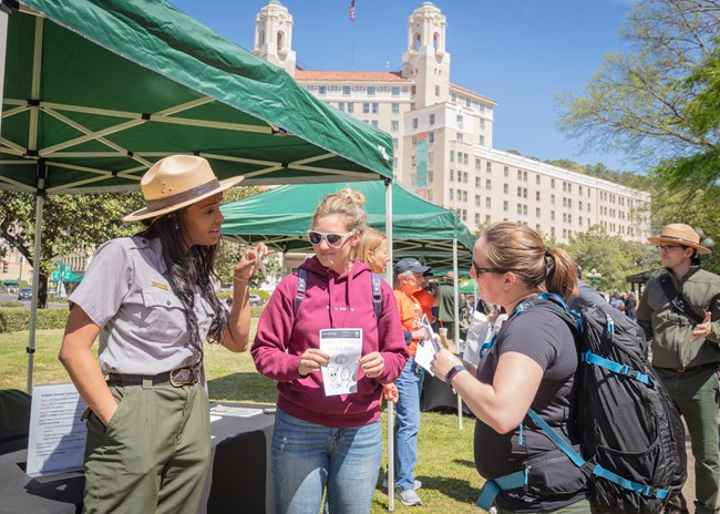 A ranger in a grey uniform speaks to a group of people at an outdoor event.