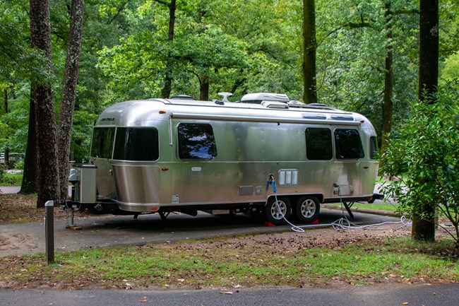 A Silver Airstream camper parked in Gulpha Gorge Campground under a green canopy of trees