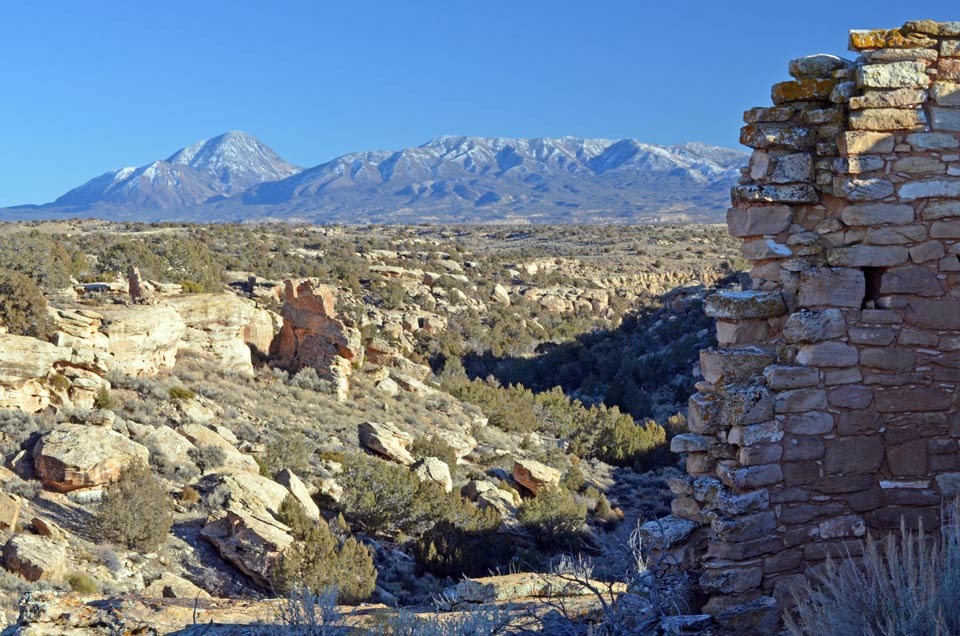 crumbling wall of sandstone ruin with shallow canyon and mountain in the background