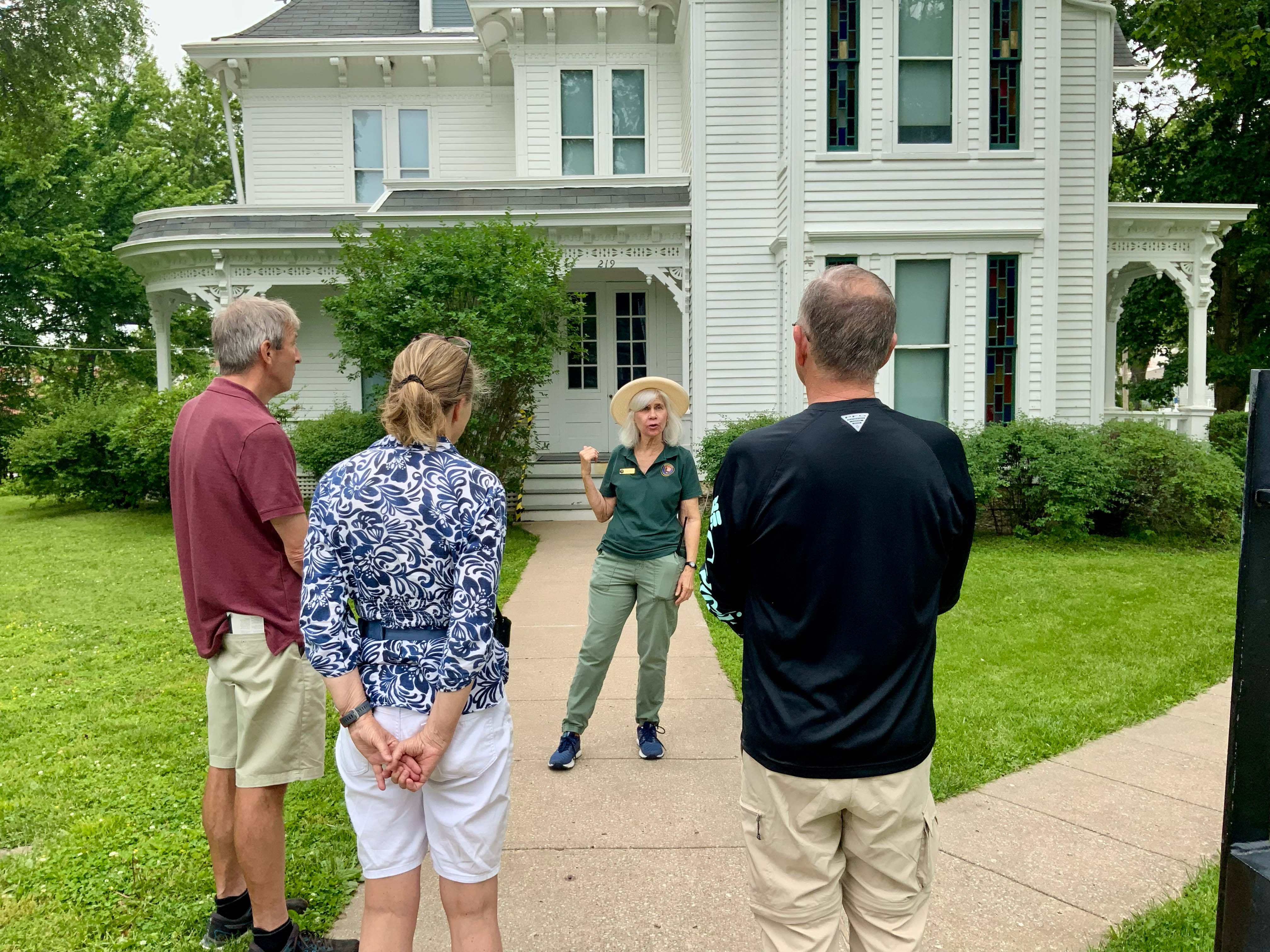 A volunteer stands in front of the Truman home talking to three visitors.