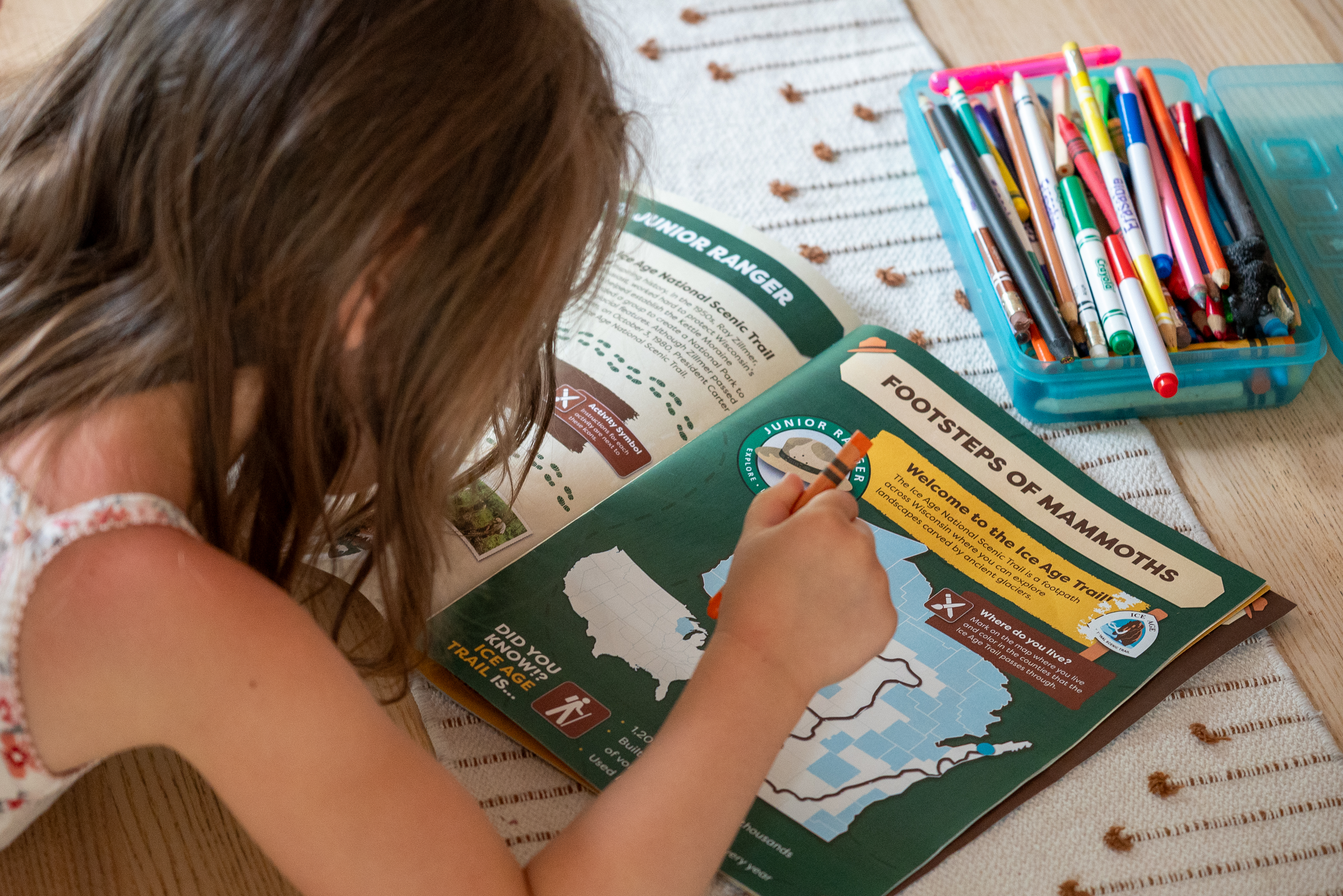 Photograph of child holding crayon and leaning over activity booklet on table.