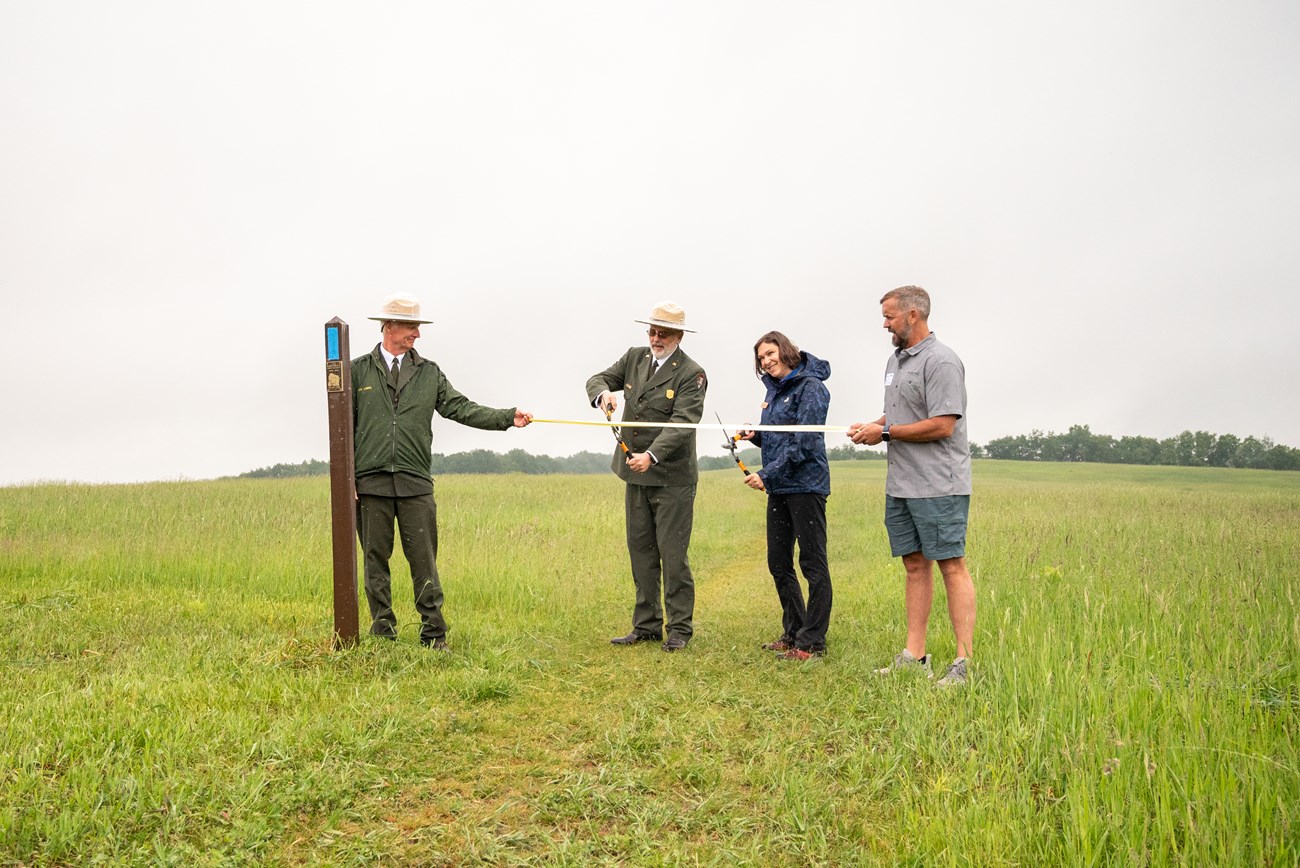 A photograph of people participating in a ribbon-cutting ceremony in a grassy field.