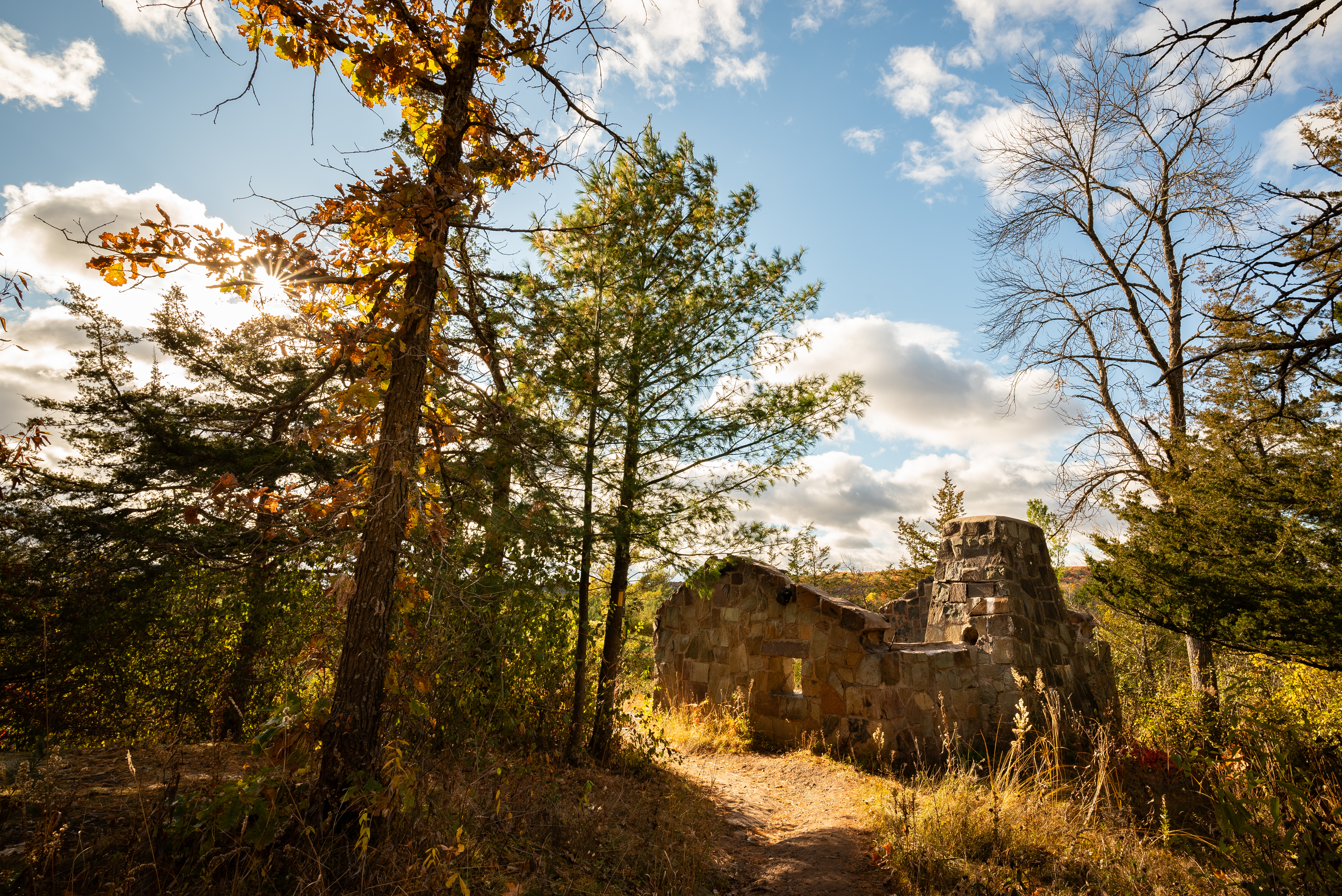 Photograph of trail through woods with the ruins of a stone building visible in the middleground.