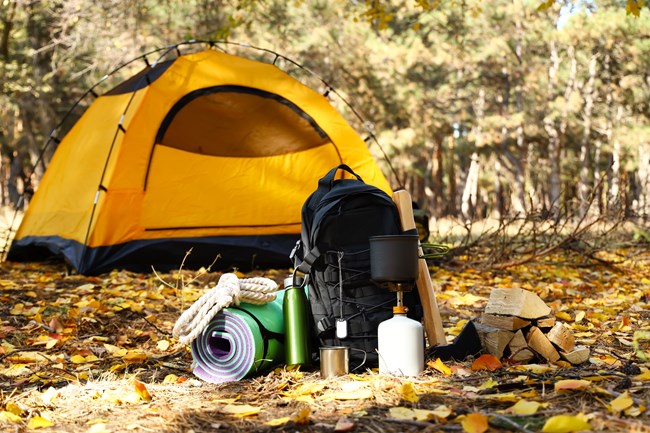 Photograph of backpack and camping supplies in front of tent in the woods.
