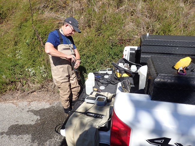 Field crew member works on a sonde at the back of truck.