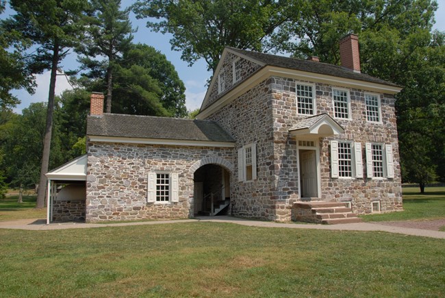 Two-story historic stone house with white trim, surrounded by grass and some trees