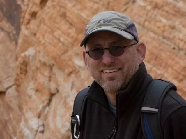 Smiling man in baseball cap and dark glasses with sandstone formation behind him