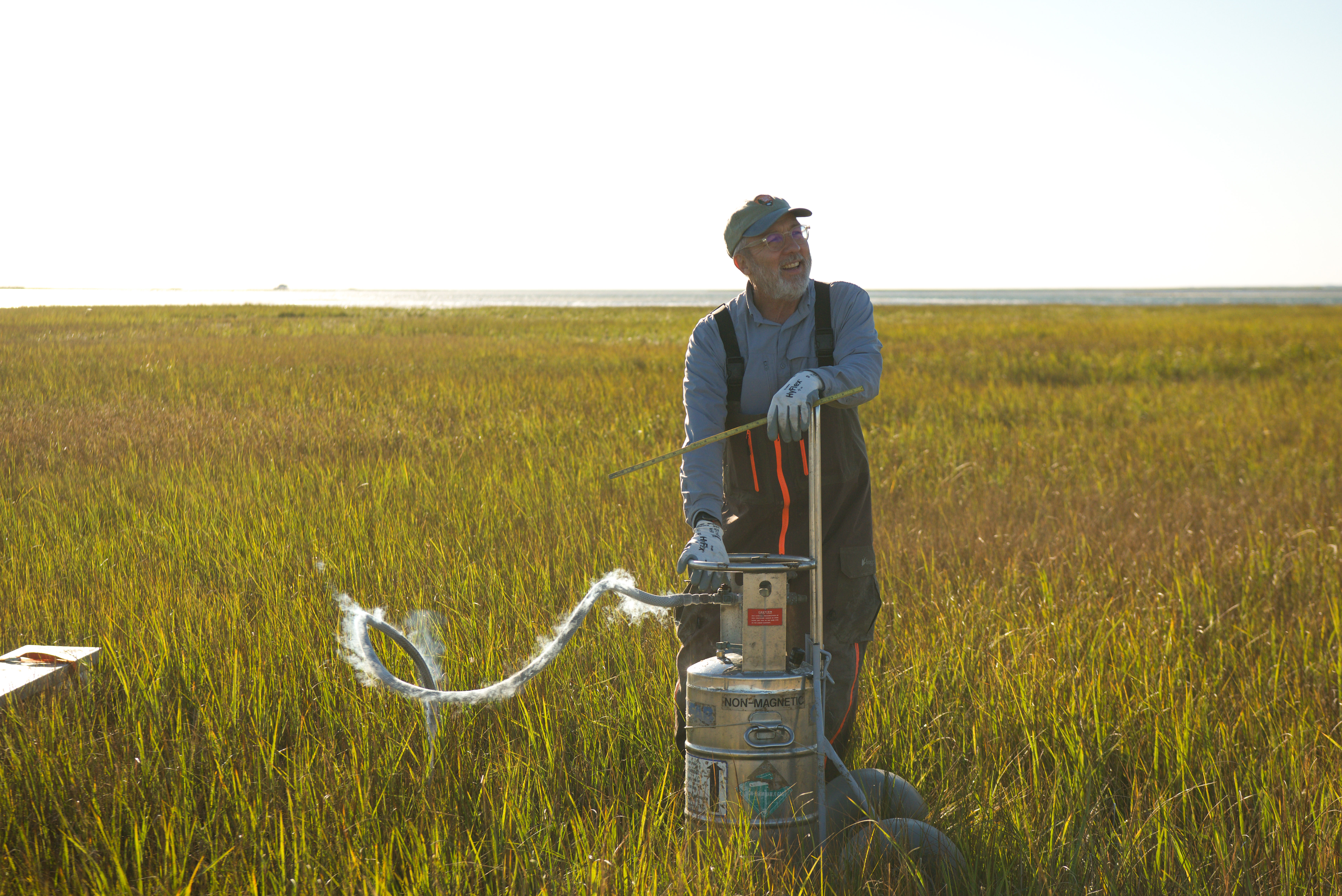 A field crew member stands next to a metal barrel with a tube that has steam rising from it