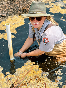 Katie installs a water logger in a marsh.