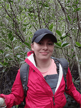 Laura stands in front some vegetation.