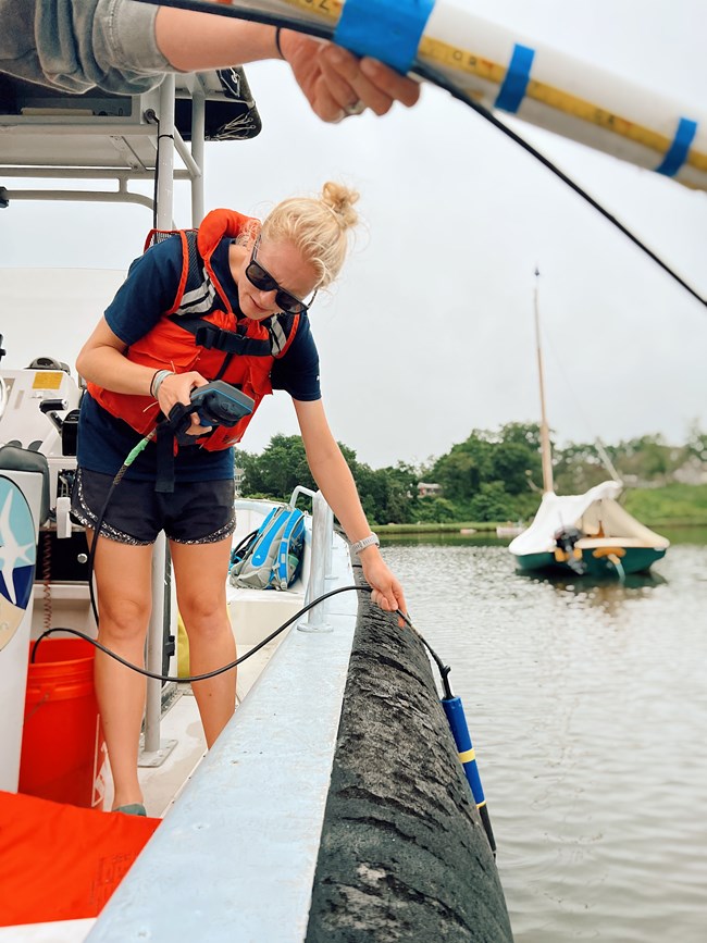 Scientist holds water quality monitoring equipment off the side of a boat.