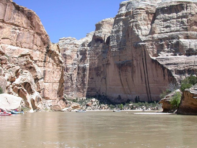 Rafts float on the Yampa River beneath towering canyon walls.