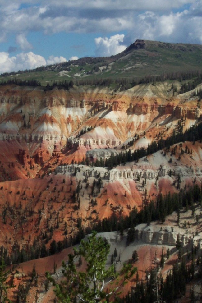 Brian Head Peak behind Cedar Breaks’ colorful cliffs, with lingering snow and conifer forest.