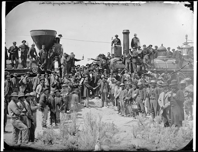 Railroad workers and officials gathered between two locomotives for the Golden Spike ceremony