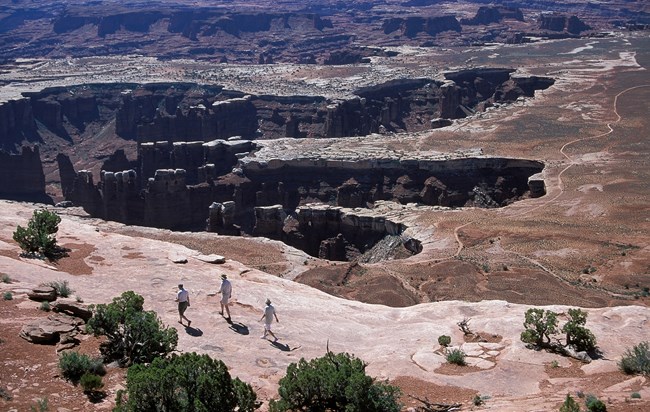 Group of hikers on canyon rim trail with panoramic views in Canyonlands National Park.