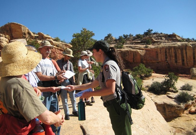 Ranger handing out materials to visitors on a guided hike in a rocky desert setting.