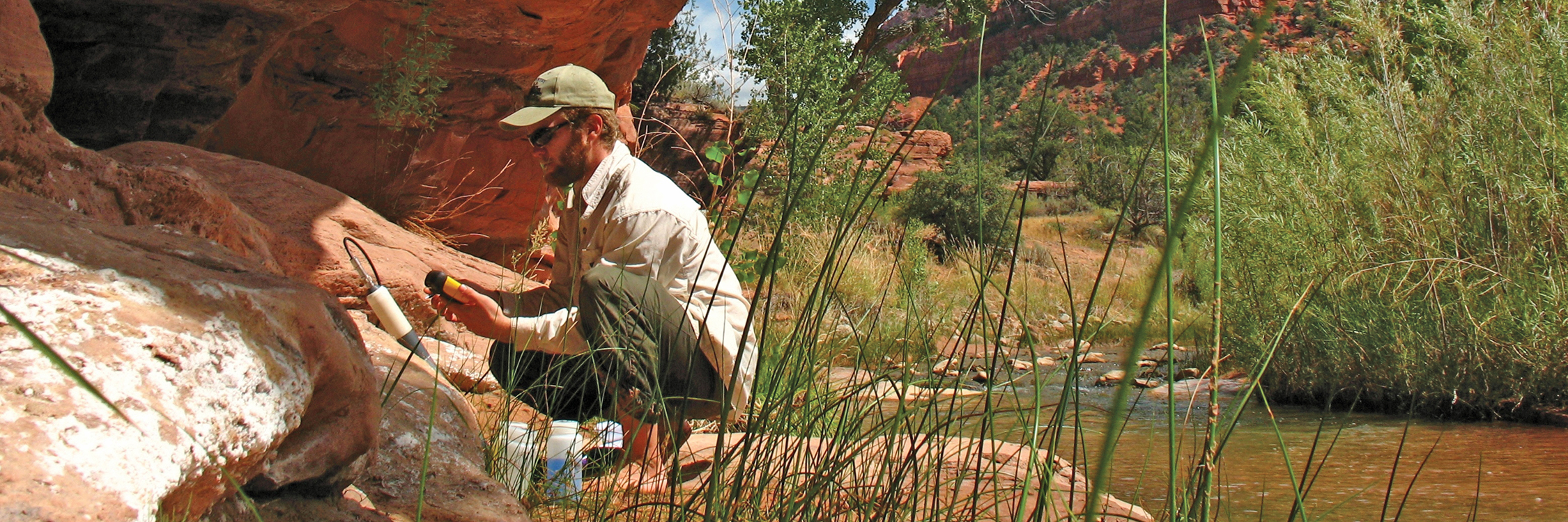 Man crouches at edge of La Verkin Creek with sonde and sampling bottles.