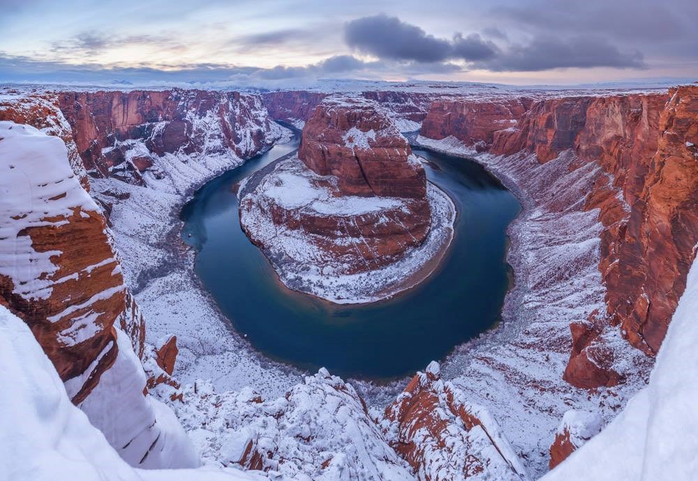 Looking down at a large bend in a river, with canyon walls covered in snow.