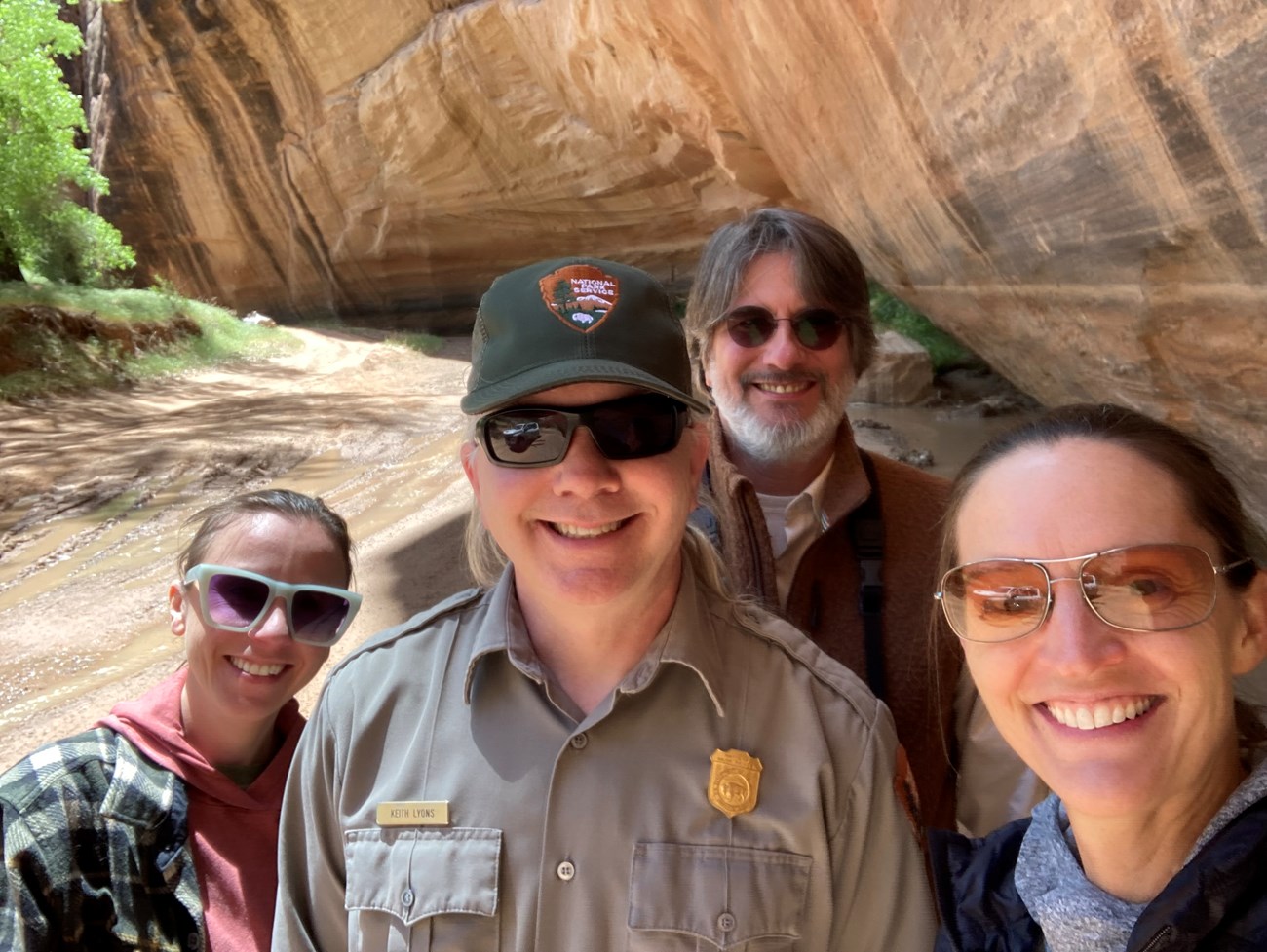 Four people grouped together and smiling in a dry wash at the bottom of a sandstone canyon.