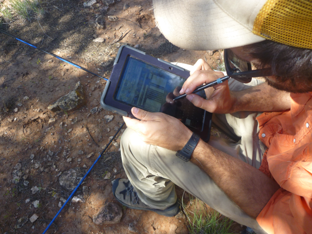 Man in orange shirt and beige pants entering data on a tablet.