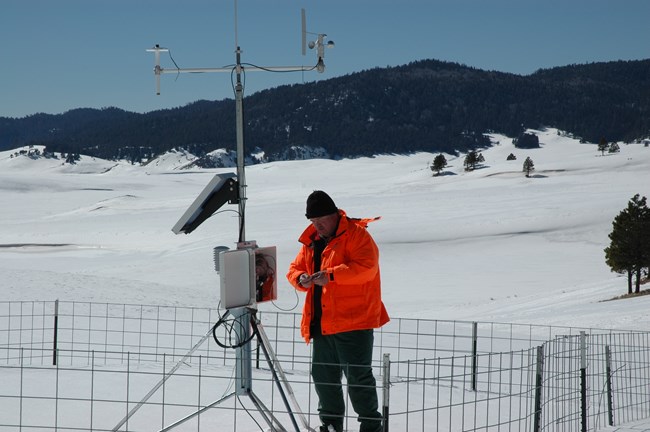 Person in orange jacket reading data off a machine in the snow.