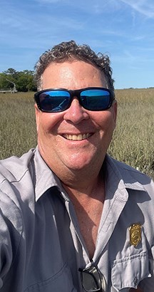 Man in sunglasses standing in a marsh, smiling