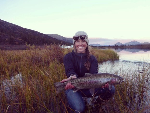 A woman with a beanie and sunglasses holds a large colorful fish