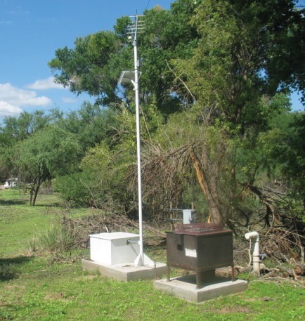 Two metal boxes sit on concrete pads near a copse of trees.