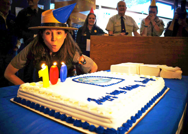A uniformed female park ranger blows out the candles on Rocky's 100th birthday cake