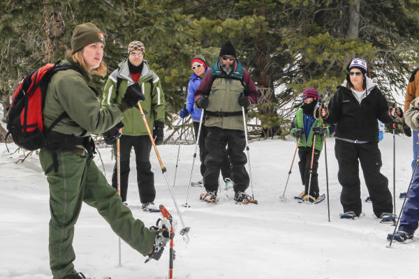 A ranger and visitors lift up their snowshoe-shod feet while standing on snow