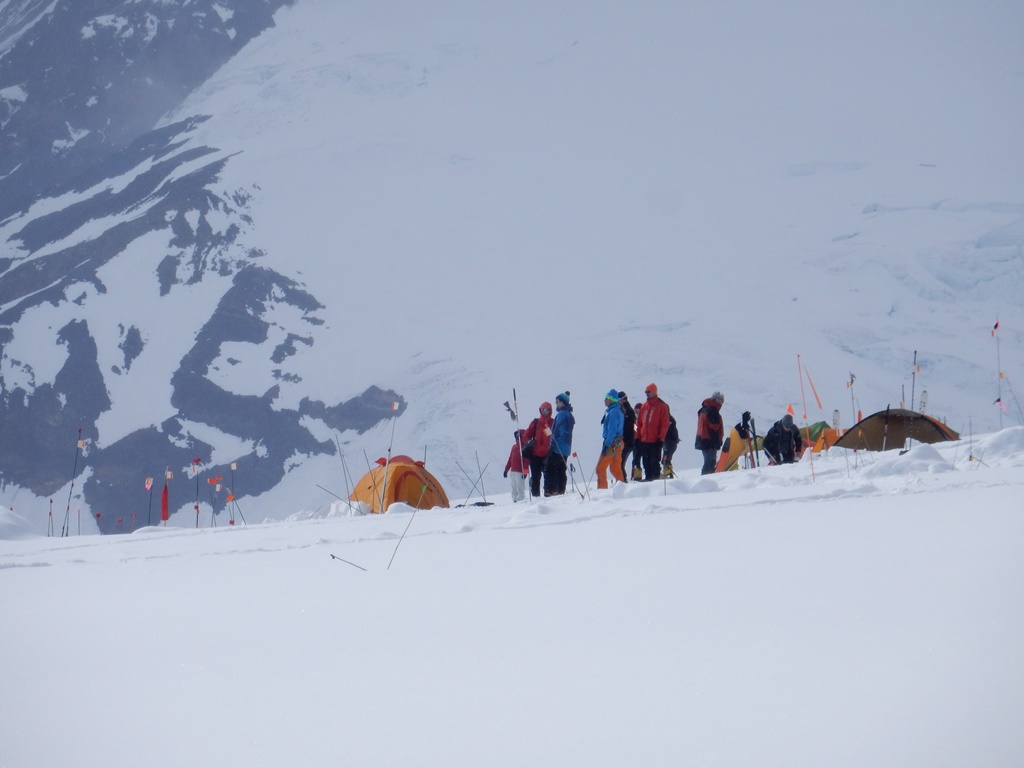 Brightly clothed climbers watch aircraft land at the Kahiltna Glacier