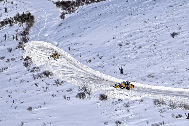 two yellow machines pushing snow around in a frozen landscape, revealing a dirt road