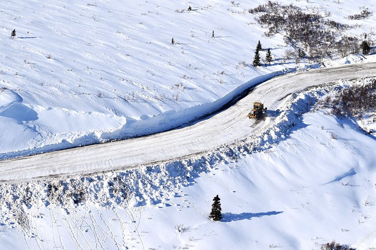 aerial view of a plow driving down a snowy road in a snowy landscape