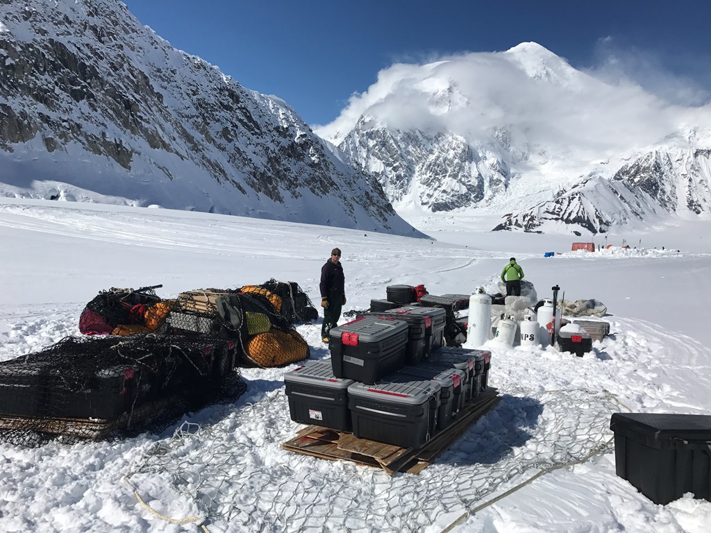 A stack of gear and action packers sit on a glacier waiting to get ferried to 14,200 feet