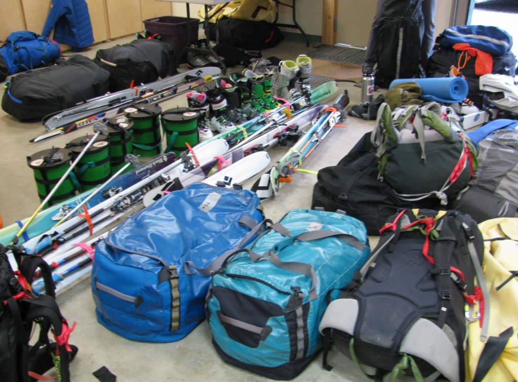 a pile of mountaineering gear, including duffels, skis, backpacks, CMCs and other gear