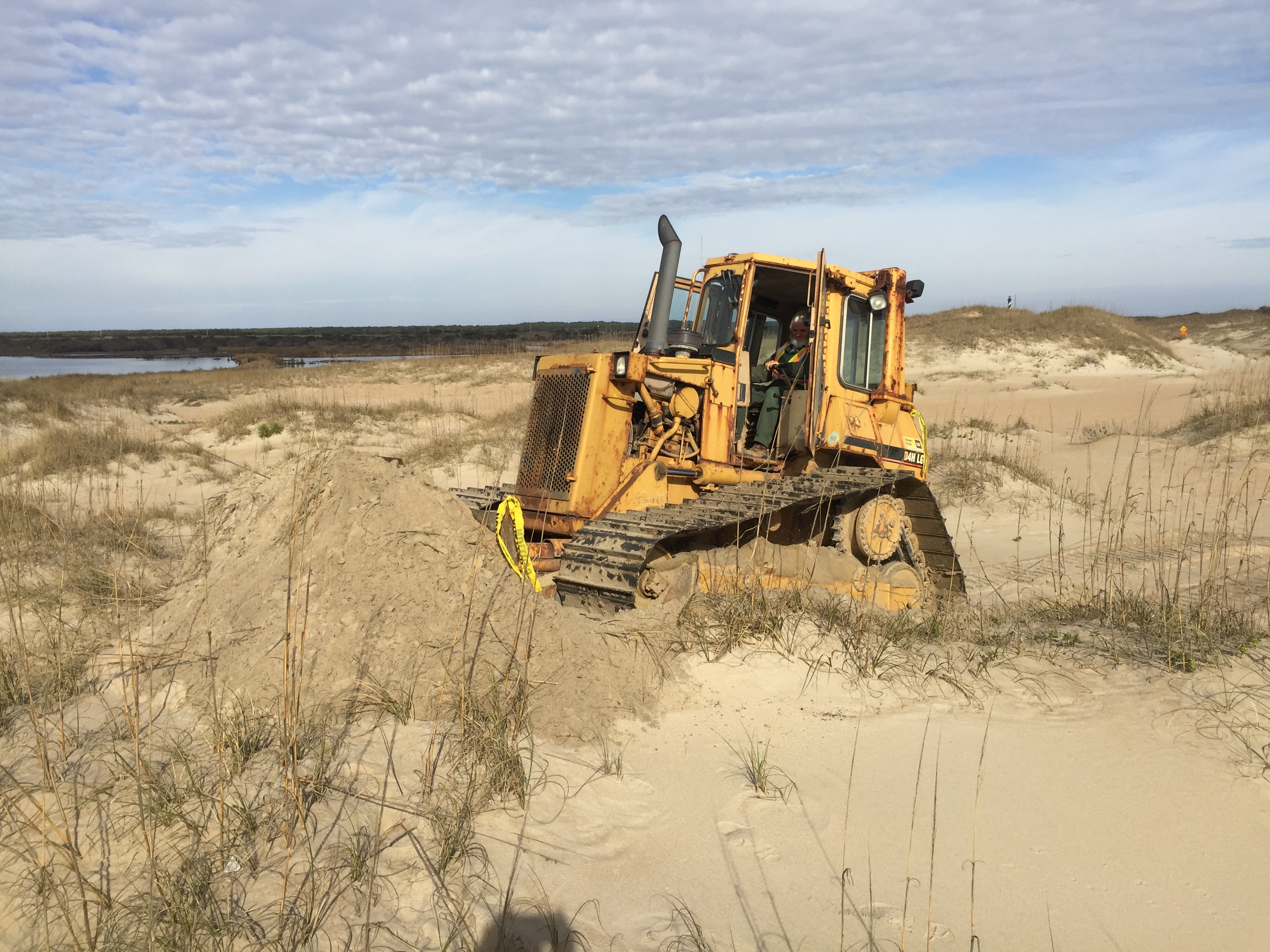 Heavy equipment operator beginning work on Cape Point bypass. Cape Hatteras Lighthouse in background.