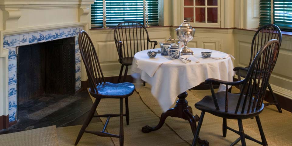 Windsor chairs surround a round table near a fireplace.