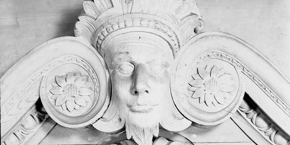 Black and white photo showing close-up of carved mask that looks like a face.