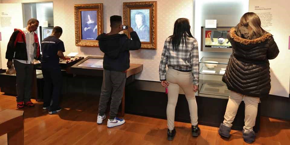 Color photo of five teens with their backs to the camera, looking at the exhibits in the Benjamin Franklin Museum