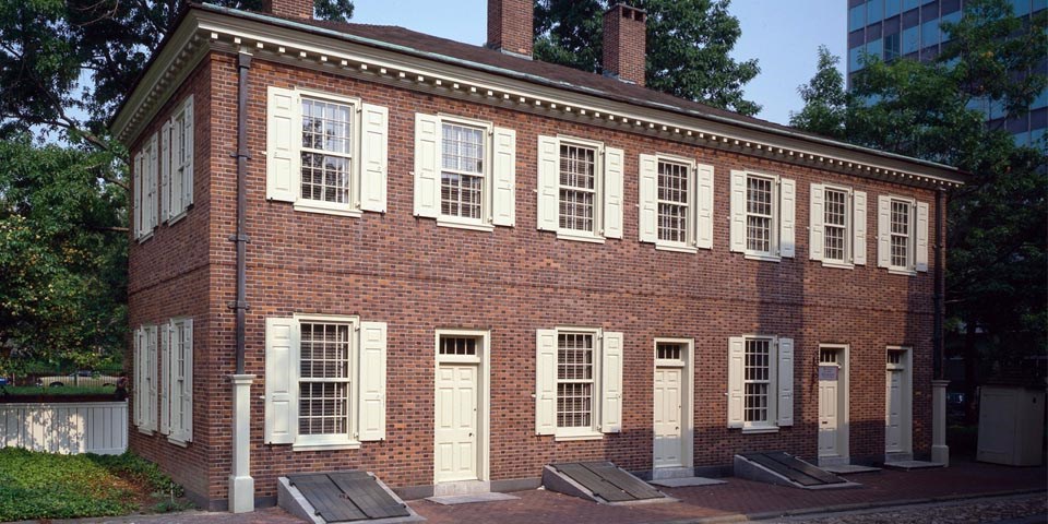 Color photo of the exterior of the New Hall Military Museum, a two story red brick building, rectangular in shape with rows of windows flanked by cream shutters.