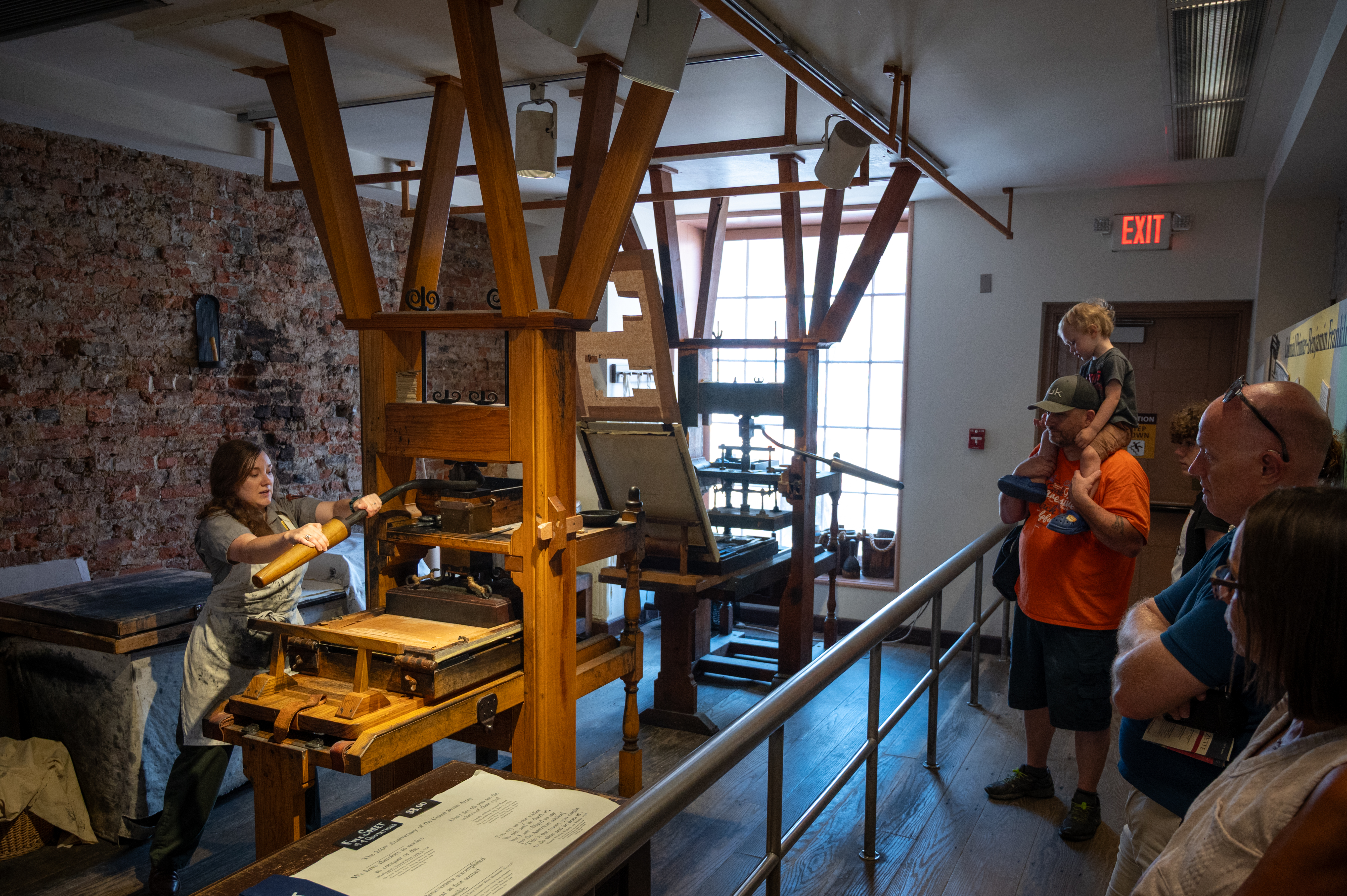 Woman demonstrating the printing process on an 18th century style printing press