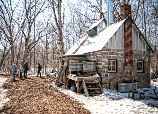 Cement block structure with metal roof and brick chimney in a snowy woodland scene.