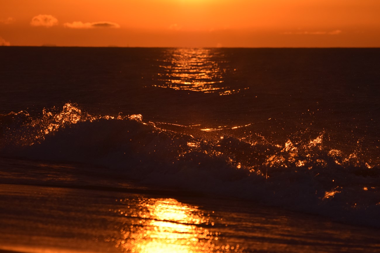 Orange sunset light filters through a splashing wave of Lake Michigan