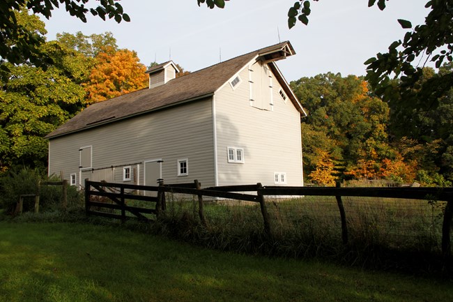 Large, gray, wooden barn among trees with fall colors.